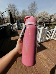 a person holding a pink water bottle on top of a wooden deck