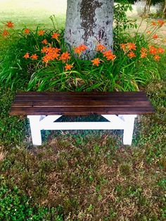 a wooden bench sitting in front of a tree and some flowers on the side of it