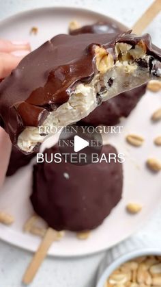 a person is holding an ice cream bar on a white plate with nuts in the background