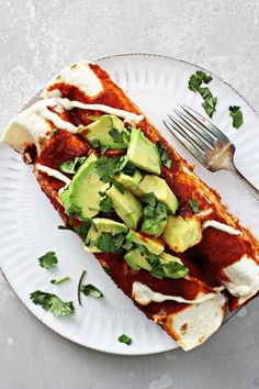 a white plate topped with chicken enchiladas covered in sauce and avocado