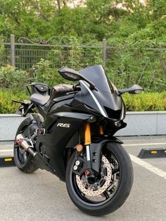 a black motorcycle parked in a parking lot next to some bushes and trees on either side of the road