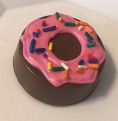 a chocolate donut with pink frosting and sprinkles sitting on a white surface