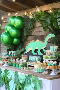 a dinosaur themed birthday party with green balloons and desserts on the table, including cupcakes