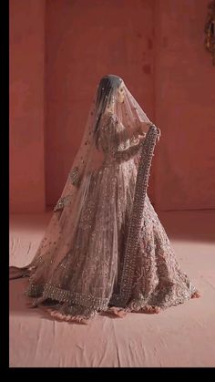 a woman in a bridal gown and veil is sitting on a pink floor with her back to the camera