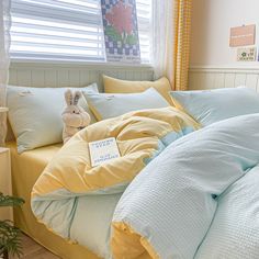 a bed with blue and yellow comforters in front of a window, next to a potted plant