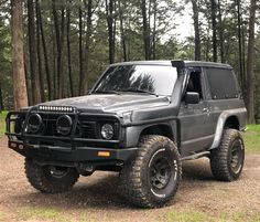 a gray truck parked on top of a dirt road next to trees in the forest