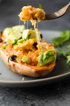 a fork is lifting up some food from a stuffed sweet potato on a plate with avocado and black beans