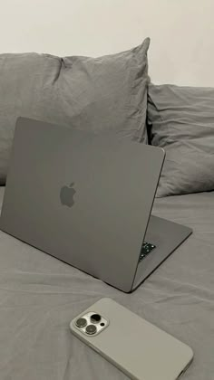 an apple laptop sitting on top of a bed next to a cell phone and pillow