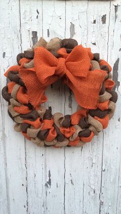 an orange and brown wreath with a bow on the side of a wooden door,