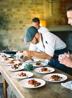 two men in aprons are preparing food at a table with plates and bowls on it