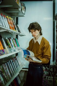 a man reading a book in front of a shelf full of books and magazines on shelves