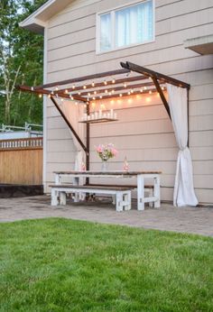 a white table and bench under a canopy with lights hanging from it's sides