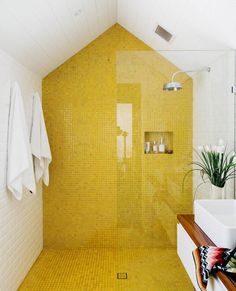 a yellow tiled bathroom with white towels and plants in the window sill next to the shower