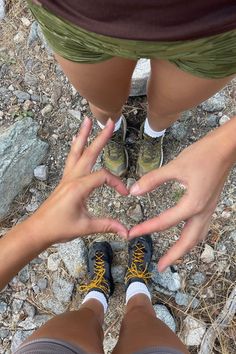 two people making a heart shape with their hands while standing on the ground in front of some rocks