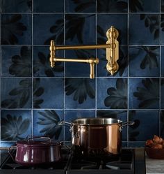 a pot is on the stove in front of a blue tiled wall with gold accents