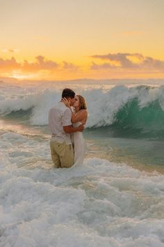 a man and woman standing in the ocean with their arms around each other as they kiss