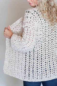 a woman wearing a white crochet cardigan sweater and jeans, with her hands on her hips