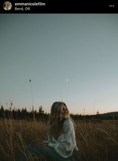 a woman sitting in the middle of a field with her hair blowing in the wind