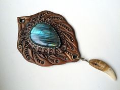 "\"Restless soul\" is a hand tooled leather fantasy pendant in blue-bronze palette with iridescent labradorite cabochon as a central piece. Glossy iridescent colours would drag attention to the place where this pendant hangs ;) This pendant reminds me of wild wild West and its legends. Pendant looks great with western clothes, however, would make a great \"bright spot\" on any everyday clothes as well. Listing includes a bronze chain, thus please provide me with the desired length upon purchase. Bohemian Labradorite Collectible Jewelry, Handmade Brown Labradorite Jewelry, Unique Labradorite Jewelry For Festivals, Brown Patina Jewelry For Festival, Brown Jewelry With Patina For Festival, Brown Engraved Jewelry For Festivals, Brown Engraved Jewelry For Festival, Hand Tooled Leather Bohemian Jewelry, Unique Leather Jewelry For Festivals