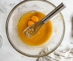 two eggs are being whisked together in a bowl with orange liquid and an electric whisk