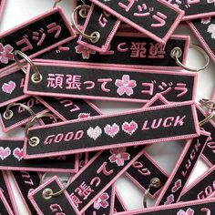 pink and black keychains with japanese characters on them are laid out in rows