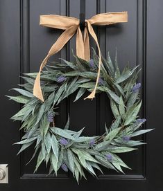 a wreath is hanging on the front door with a tan ribbon and some purple flowers