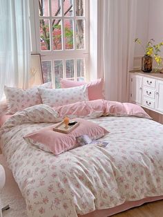 a bed with pink comforters and pillows in a white room next to a window