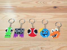 four pixel keychains are shown on a wooden surface, each with different characters