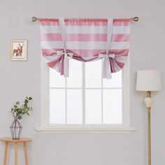 a pink and white striped window curtain in a living room with a lamp, table, and pictures on the wall