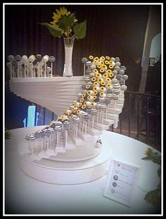 a white table topped with a vase filled with sunflowers next to a spiral staircase