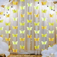 some white balloons and yellow butterflies are hanging from the ceiling in front of a curtain