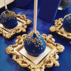 three blue cake pops with gold sprinkles on them sitting in golden frames