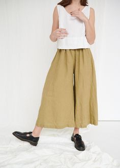 "The Clementine palazzo is the right choice for warmer days when you want to give a romantic touch to your look. The pants boast a cropped hem, in-seam pockets and a flattering gathered skirt-like high waist with an elastic band in the back. IMPORTANT: The Clementine pants have been altered to have a gathered waist instead of the pleated one. If you own a pair with pleated front, note that the pants you will receive will be different. This garment is true to size, and we recommend choosing the s Olive Wide Leg Pants For Spring, Olive Wide Leg Pants With Elastic Waistband, Chic Olive Summer Pants, Olive Wide Leg Relaxed Fit Pants, Olive Wide-leg Spring Pants, Olive Wide Leg Summer Bottoms, Olive Wide-leg Pants For Spring, Olive Wide Leg Bottoms For Summer, Olive Relaxed Fit Pants For Summer