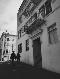 two people walking down the street in front of an apartment building with fire escape stairs