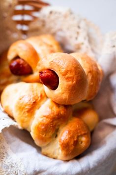 hotdogs wrapped in bread sitting on top of a white cloth next to a basket