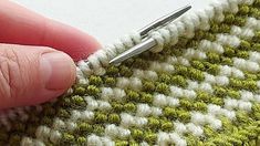 someone is crocheting the stitchs on a green and white knitted blanket