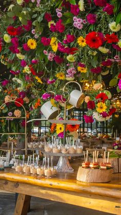 a wooden table topped with lots of desserts under a hanging flower filled ceiling covered in flowers