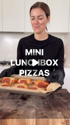 a woman in black shirt holding a pan with pizza on it and the words mini lunchbox pizzas