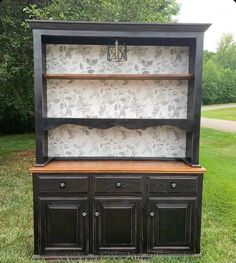 an old china cabinet is painted black and has floral wallpaper on the top shelf