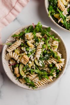 two bowls filled with pasta and greens on top of a white countertop next to a pink towel