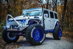 a white jeep with blue lights on it's tires is parked in the woods