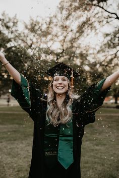 a woman in a graduation gown throwing confetti on her head and arms as she smiles