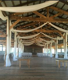 an indoor wedding venue with white draping and wooden benches in the center, surrounded by string lights