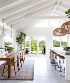 a dining room with white walls and wooden tables in the foreground is an open floor plan