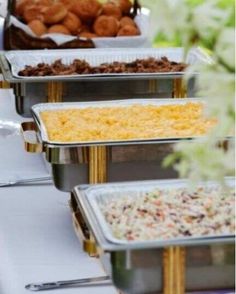 several trays of food are lined up on a buffet table with flowers in the foreground