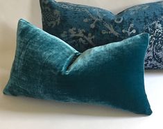 two blue pillows sitting next to each other on a bed