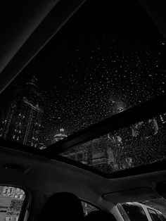 black and white photograph of rain falling on the roof of a car at night time