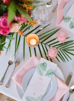 the table is set with pink and green place settings, silverware, and candles