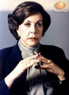 an older woman is holding her hands together and looking at the camera while wearing a scarf