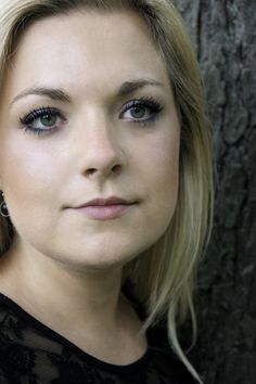 a close up of a woman near a tree with blue eyeshadow on her face